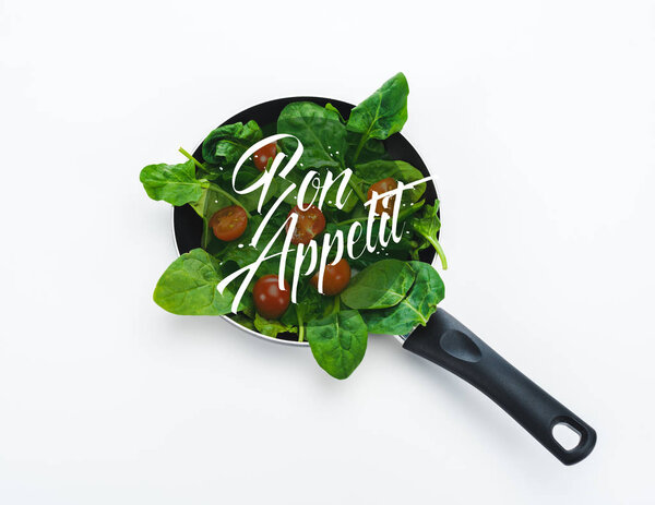 fresh spinach leaves and cherry tomatoes in frying pan with bon appetit lettering on white background