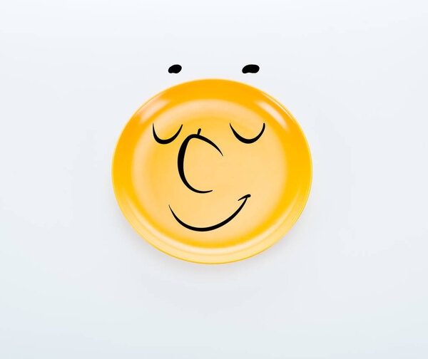 top view of shiny yellow plate with pleased smiley on white background