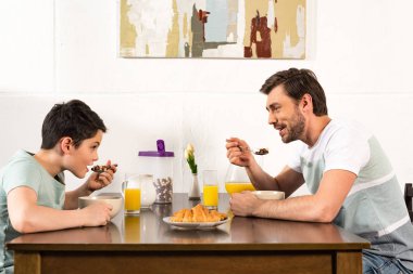 gülümseyen baba ve oğul kahvaltı ve mutfakta birbirlerine bakarak