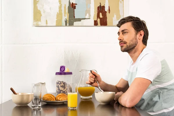 留胡子的男人坐在餐桌上 早餐和梦幻般的看远在厨房 — 图库照片
