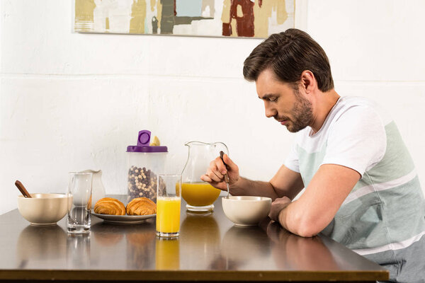 bearded man sitting at table and having breakfast in kitchen