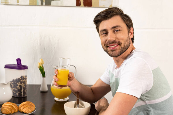 smiling bearded man holding glass of orange juice during breakfast