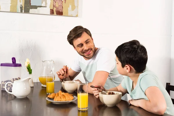 微笑的父亲和儿子吃早餐 看着对方在厨房 — 图库照片