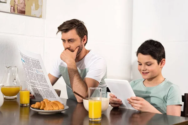 Padre Pensativo Leer Periódico Hijo Usando Tableta Digital Durante Desayuno — Foto de Stock