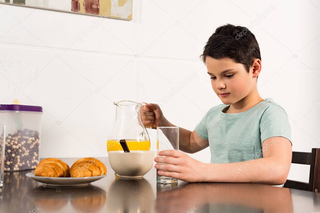 boy holding glass and jug with orange juice in kitchen