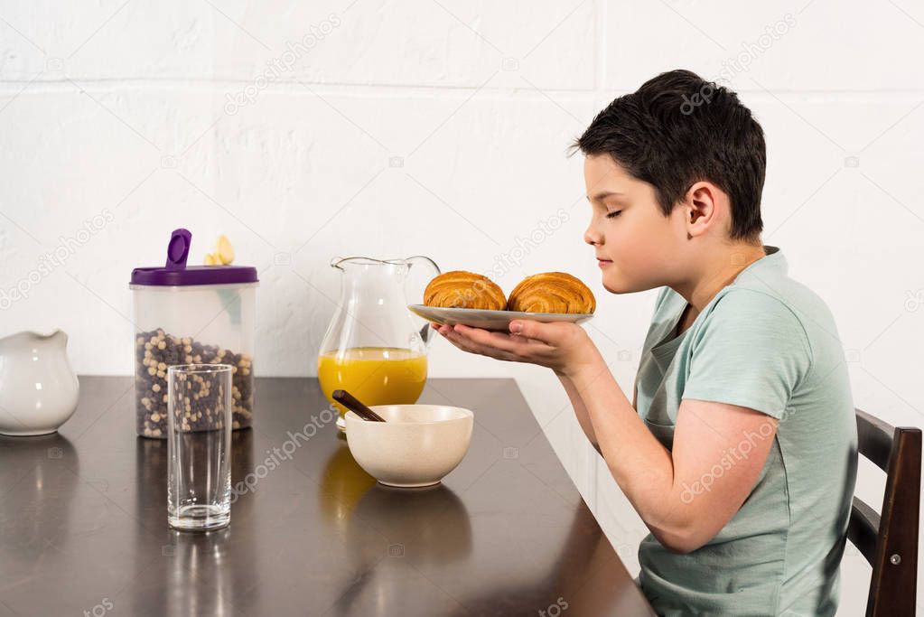 boy sniffing croissants with closed eyes during breakfast in kitchen