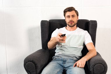 koltukta oturan ve uzaktan kumanda tutan kot adam