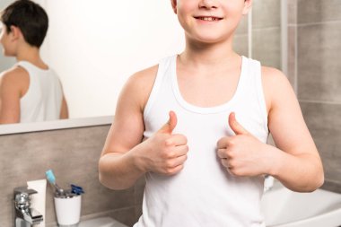 cropped view of smiling boy showing thumbs up in bathroom clipart