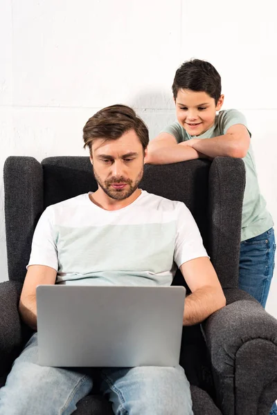 Sorridente Figlio Guardando Padre Che Utilizza Computer Portatile Soggiorno — Foto Stock