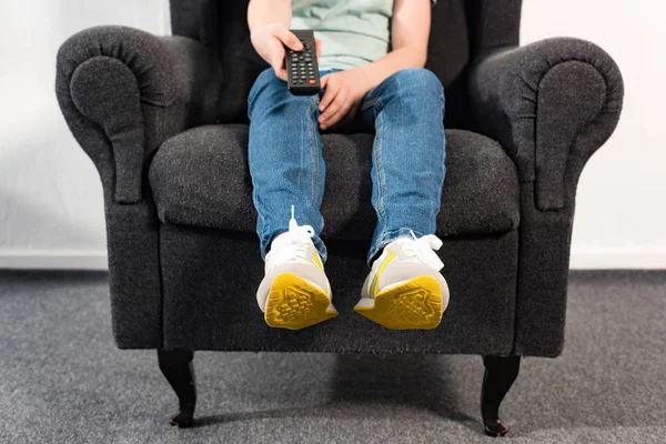 穿牛仔裤的男孩坐在扶手椅上 拿着遥控器 — 图库照片