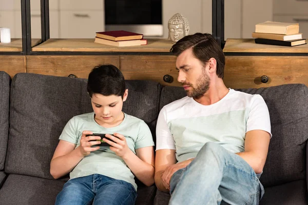 Dad Looking Son Using Smartphone While Sitting Sofa Living Room — Stock Photo, Image