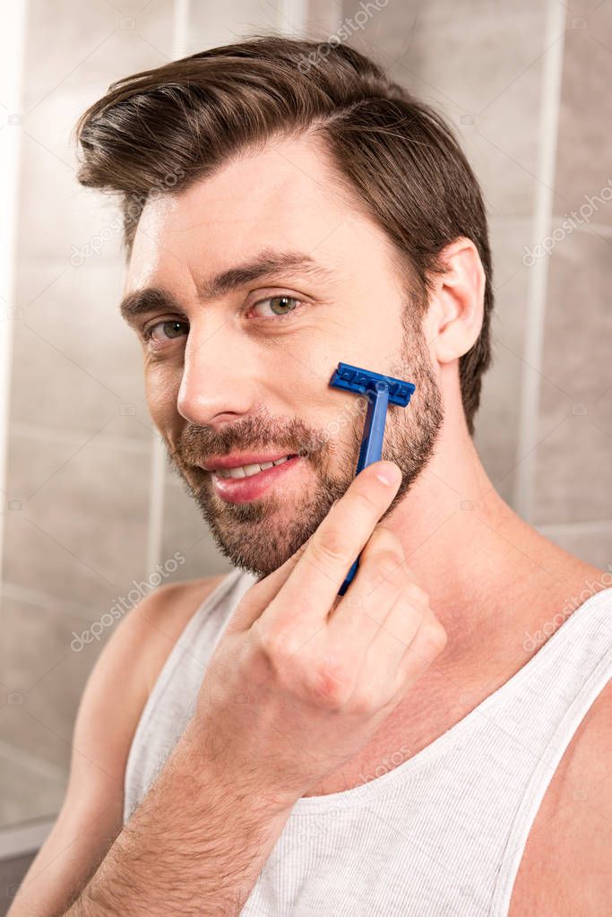 handsome man shaving beard with razor in bathroom