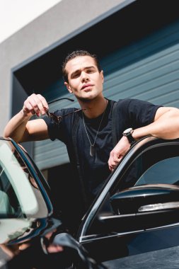 yakışıklı şık adam araba yaslanmış ve garaj yakınında poz