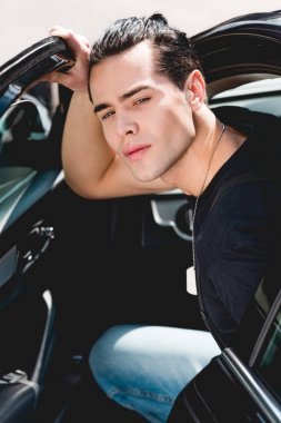 yakışıklı şık adam kameraya bakıyor ve arabada otururken poz 