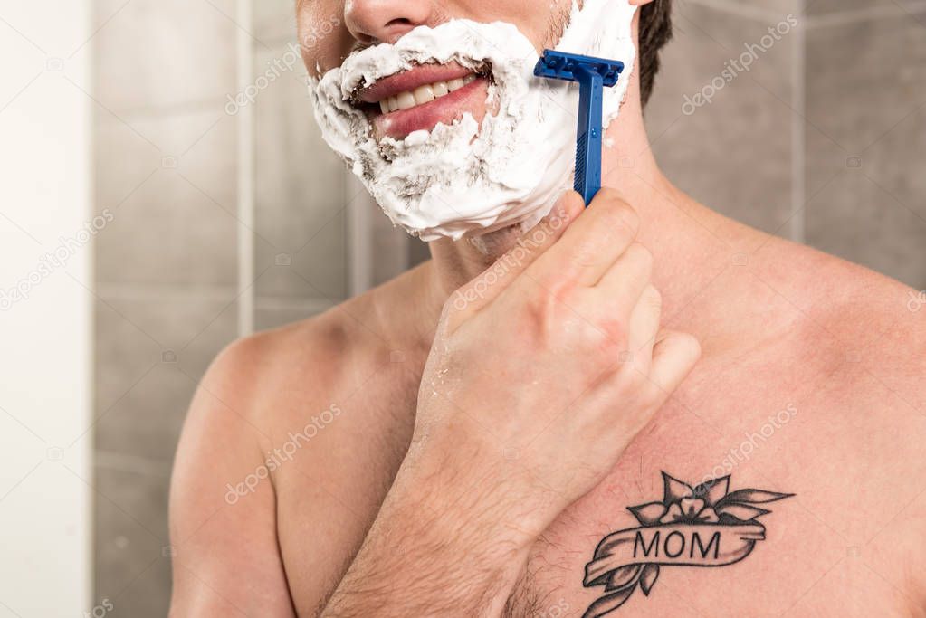 cropped view of smiling man shaving beard with razor in bathroom