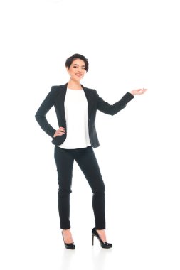 gülümseyen karışık ırk iş kadını kalça üzerinde el tutarak ve beyaz izole kamera bakarken gesturing