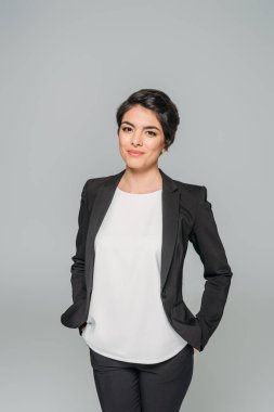güzel karışık ırk iş kadını cebinde elleri ile ayakta ve gri izole kamera gülümseyerek