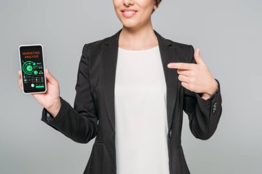 gri izole ekranda pazarlama analizi uygulaması ile akıllı telefon gösteren gülümseyen karışık ırk iş kadını kısmi görünümü