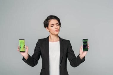 Genç melez ırk şüpheci iş kadını elinde en iyi alışverişi yapan akıllı telefonlar ve gri ekrandaki rezervasyon uygulamalarıyla