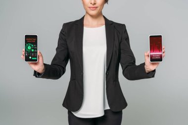 gri izole ekranda ticaret kursları ve pazarlama analizi uygulamaları ile akıllı telefonlar tutan karışık ırk iş kadını kısmi görünümü