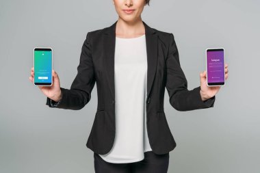 KYIV, UKRAINE - APRIL 24, 2019: Cropped shot of mixed race businesswoman showing Twitter and Instagram apps on screen isolated on grey. clipart