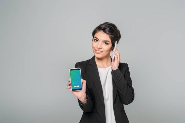 Kiev, Ukrayna - 24 Nisan 2019: Gri üzerinde izole akıllı telefonda konuşurken ekranda Twitter uygulaması ile akıllı telefon gösteren gülümseyen karışık yarış iş kadını.