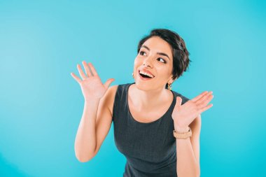 excited mixed race woman gesturing while looking away isolated on blue clipart