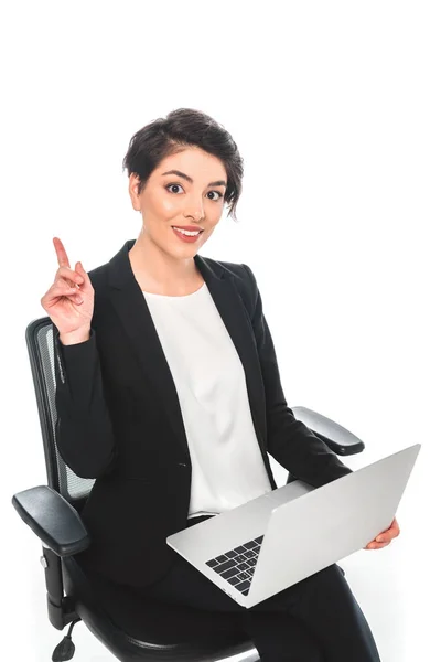 オフィスチェアに座り 白で隔離されたラップトップを使用しながら アイデアサインを示す陽気な混合レースビジネスウーマン — ストック写真