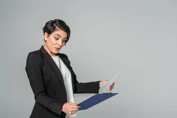 Förvånad Mixed Race Affärskvinna Tittar Urklipp Och Gest Isolerade Grått — Stockfoto