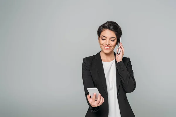Cheerful Mixed Race Businesswoman Smiling Using Two Smartphones Isolated Grey — Stock Photo, Image