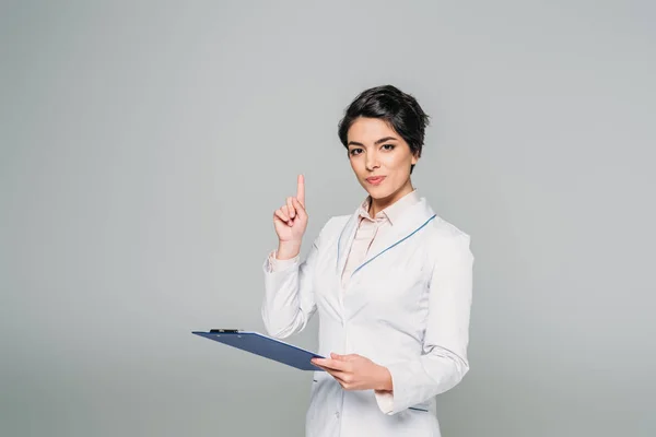 Pretty Mixed Race Doctor Showing Idea Sign While Holding Clipboard — Stock Photo, Image