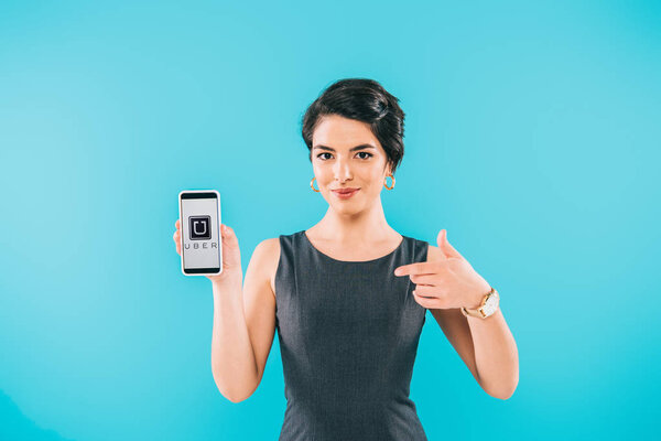 KYIV, UKRAINE - APRIL 24, 2019: Pretty mixed race woman showing smartphone with Uber app on screen isolated on blue.