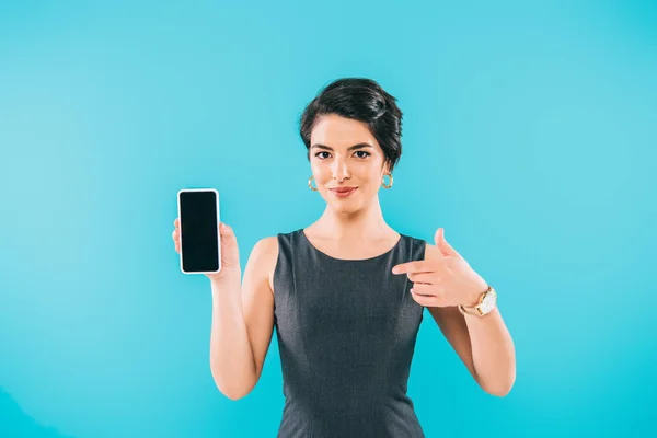 微笑的混合种族妇女指着手指在智能手机与空白屏幕隔离在蓝色 — 图库照片