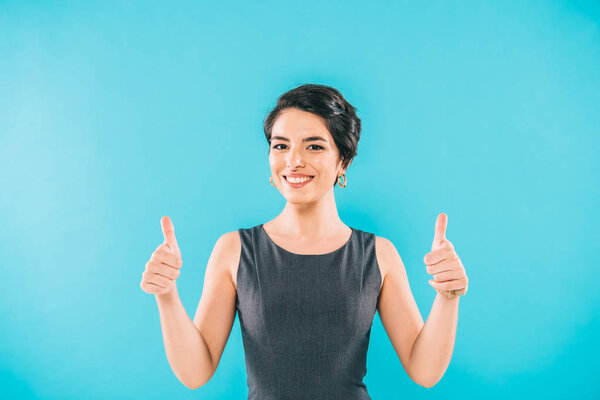 cheerful mixed race woman showing thumbs up and smiling at camera isolated on blue