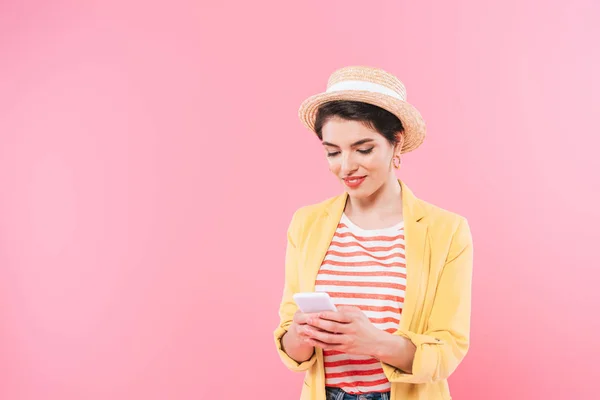 微笑混合种族女孩在明亮的衣服和草帽使用智能手机隔离在粉红色 — 图库照片