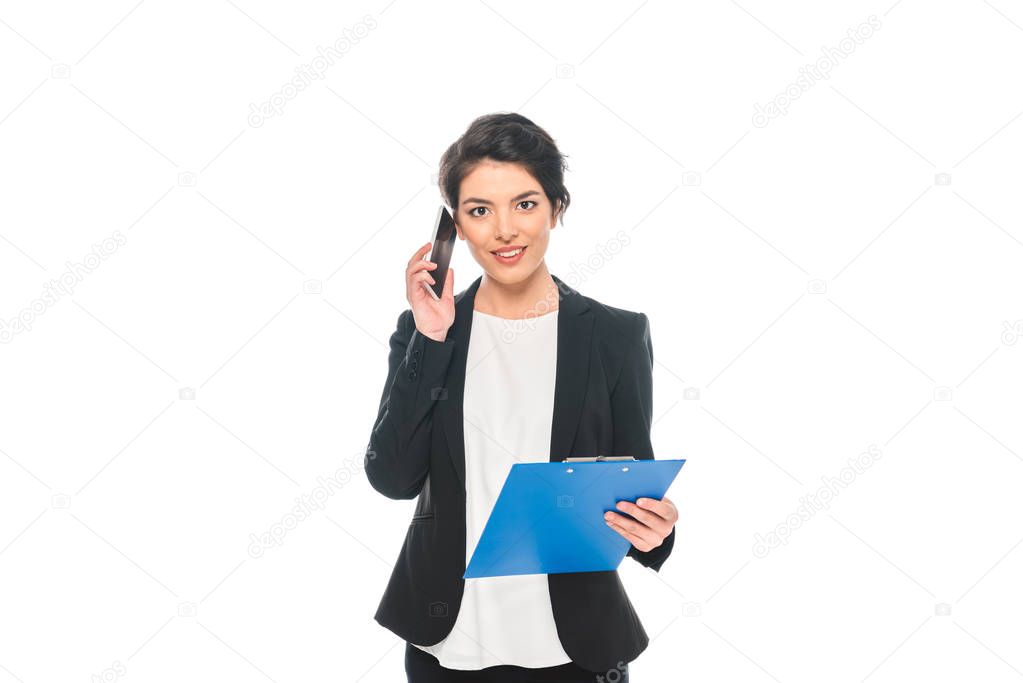 attractive mixed race businesswoman talking on smartphone while holding clipboard and looking at camera isolated on white