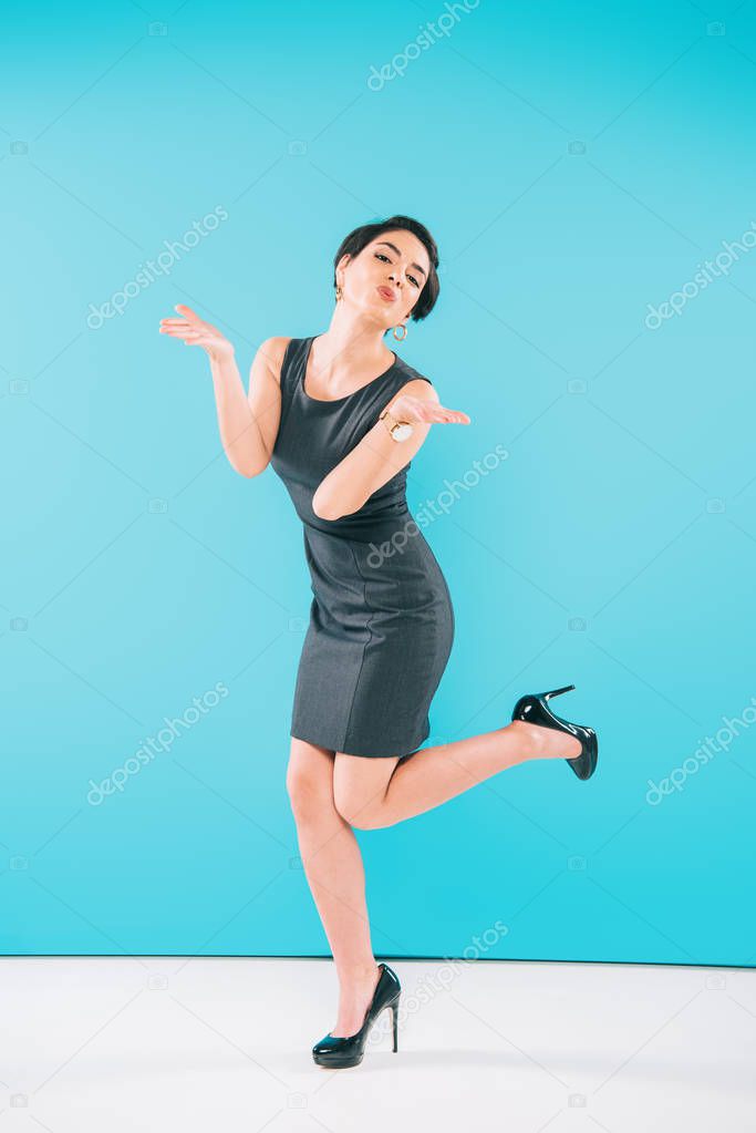 excited mixed race woman sending air kiss while posing at camera on grey background