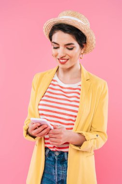 pembe izole akıllı telefon kullanarak parlak giyim ve hasır şapka gülümseyen karışık Yarış kadın