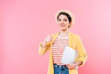 neşeli karışık yarış kadın dizüstü bilgisayar tutan ve pembe izole başparmak gösteren