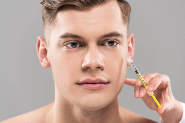 partial view of cosmetologist holding syringe and young man isolated on grey clipart