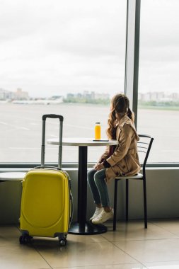 havaalanında bekleyen salonda sarı bavul yakın oturan ve pencereden bakarak preteen çocuk