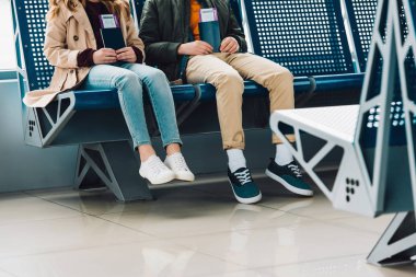Çocuklar mavi sandalyeler üzerinde oturan ve havaalanında bekleme salonunda pasaport tutarak kırpılmış görünümü
