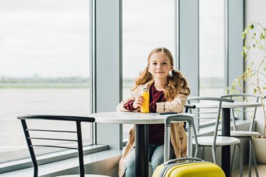 preteen çocuk havaalanında bekleyen salonda oturan, portakal suyu içme