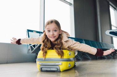 excited preteen kid lying on suitcase with outstretched hands in airport departure lounge clipart