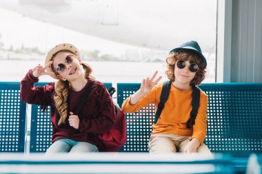 bekleme salonunda oturan ve barış işaretleri gösteren güneş gözlüğü preteen çocuklar