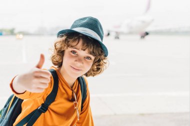 kamera bakıyor ve havaalanında başparmak yukarı gösteren preteen çocuk