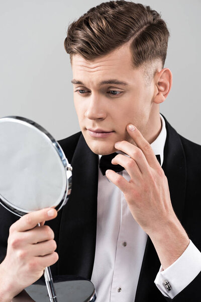молодой человек в формальной одежде, смотрящий в зеркало и трогательное лицо, изолированное на сером
