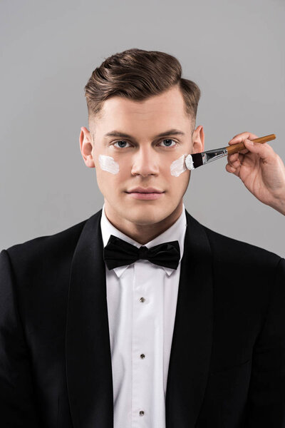 обрезанный вид косметолога, наносящего крем, и человека в формальной одежде, изолированного на сером
