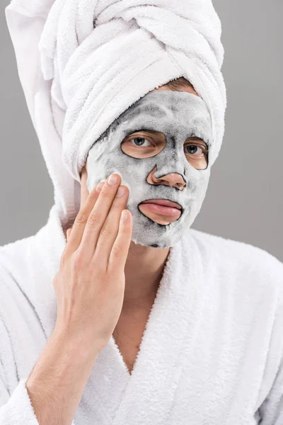 Mann Bademantel Berührt Gesichtsmaske Und Schaut Kamera Isoliert Auf Grau — Stockfoto