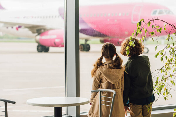 two kids standing near table and plant and looking on plane